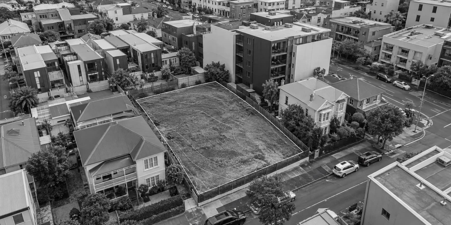 Angled aerial view of an urban infill lot among villas, townhouses and apartments, with parcel boundaries and survey contours